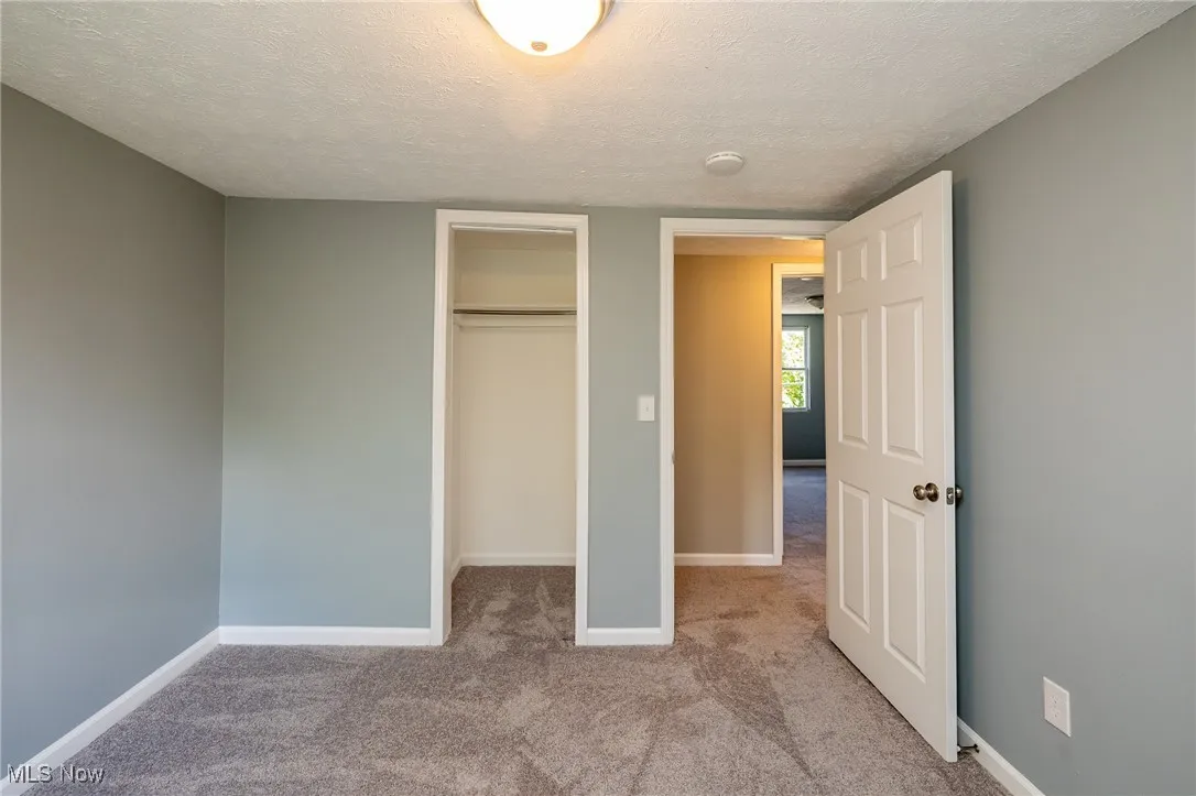 Bedroom featuring a textured ceiling, light colored new carpet, and a closet