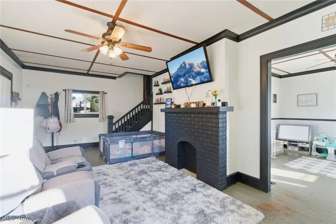 Living area with a ceiling fan, a fireplace, wood finished floors, crown molding, and stairs