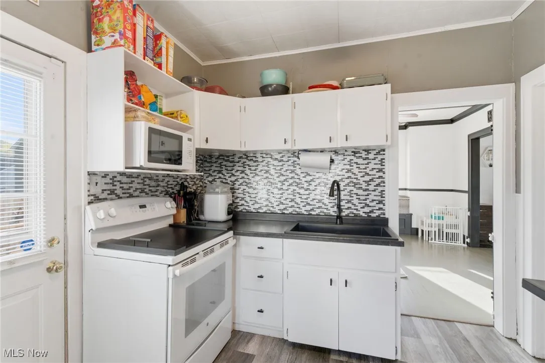 Kitchen with white appliances, white cabinets, ornamental molding, light wood-type flooring, and backsplash