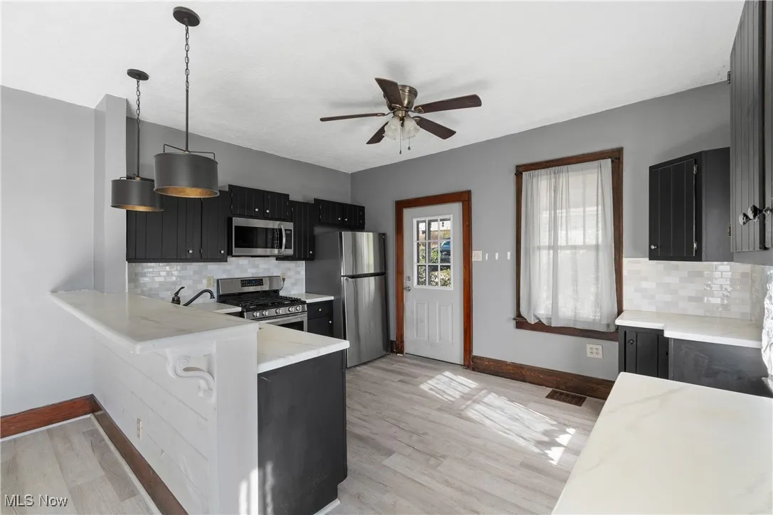 Kitchen with backsplash, dark cabinetry, hanging light fixtures, and appliances with stainless steel finishes
