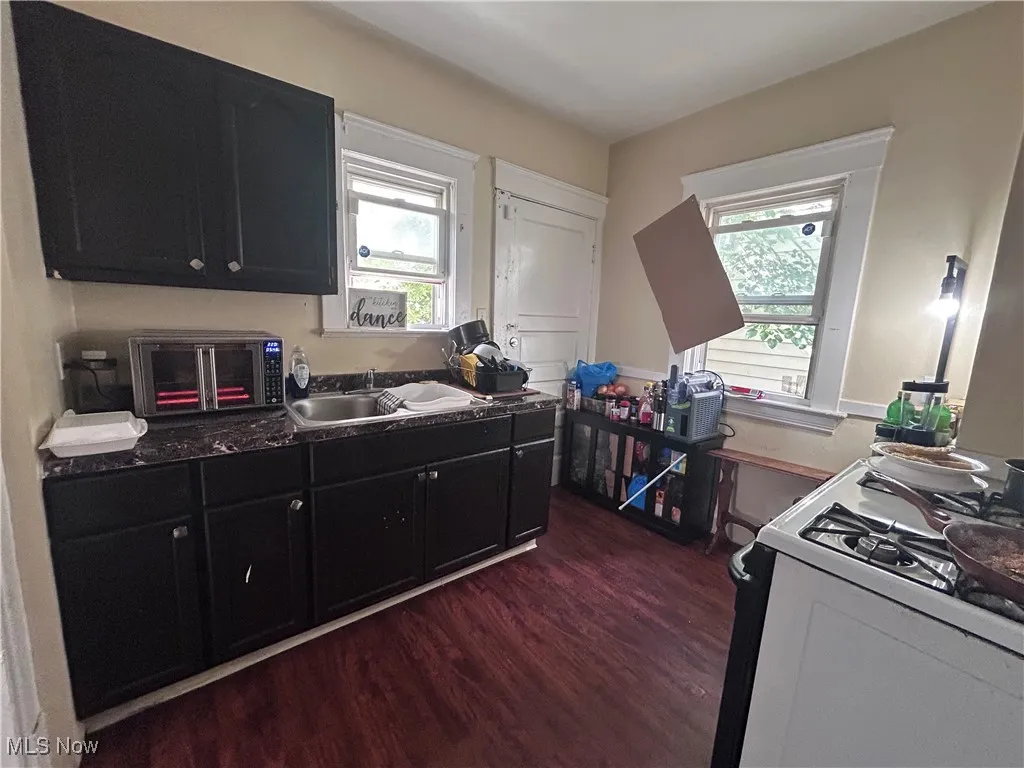 Kitchen featuring dark cabinets, white range with gas stovetop, dark wood-style flooring, and healthy amount of natural light
