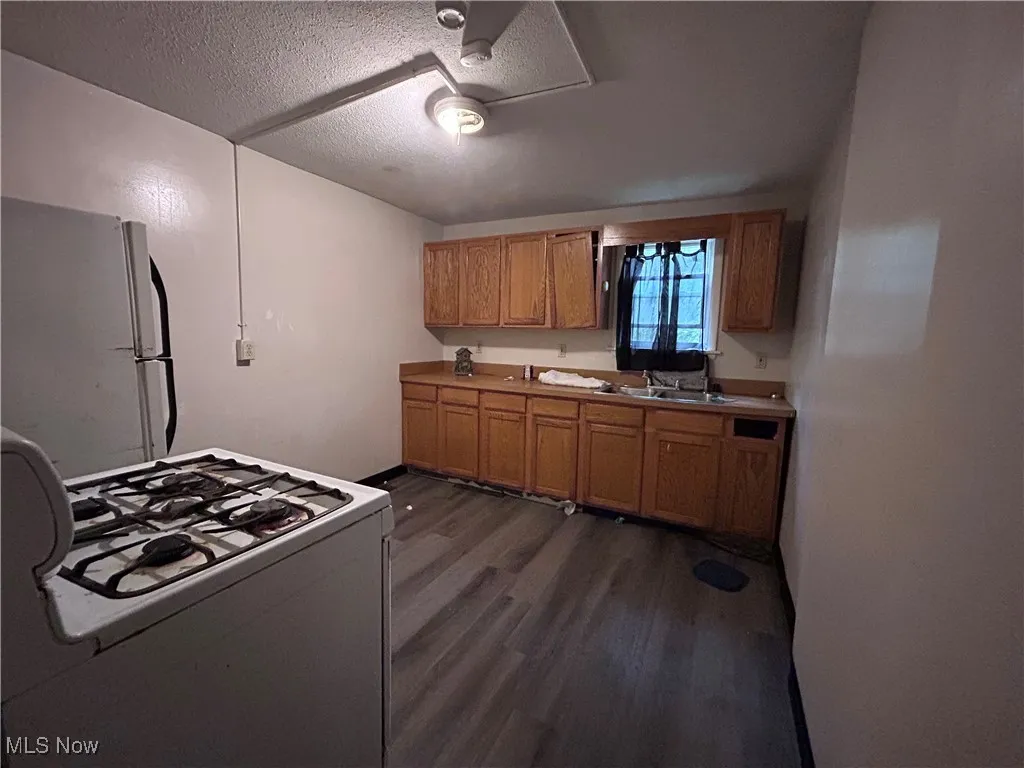 Kitchen with white appliances, dark wood-type flooring, a textured ceiling, light countertops, and brown cabinets