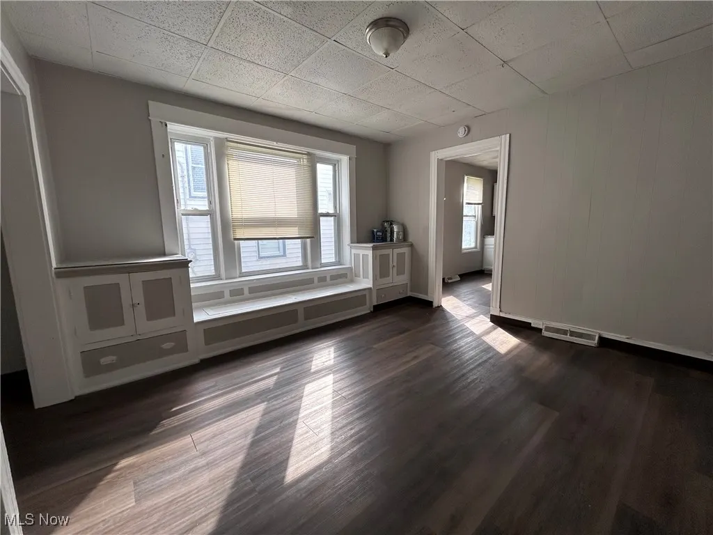 Unfurnished room with dark wood-type flooring and a drop ceiling