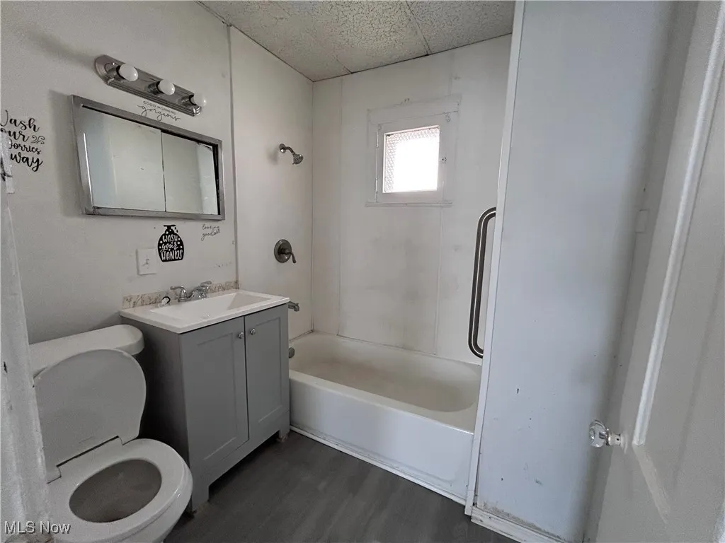 Bathroom featuring washtub / shower combination, dark wood-style floors, vanity, and a paneled ceiling