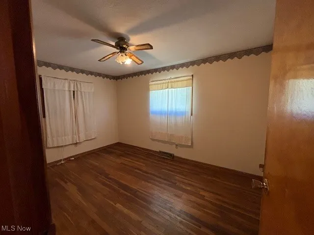 Unfurnished room featuring dark wood-style flooring and a ceiling fan