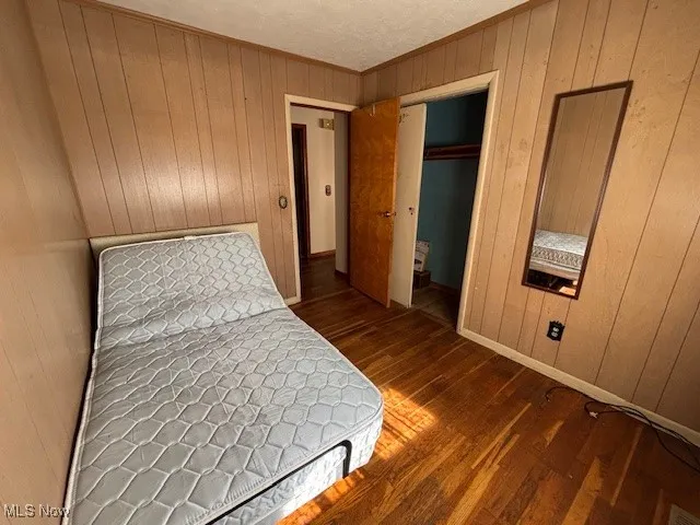 Bedroom featuring wooden walls, dark wood-style flooring, a closet, crown molding, and a textured ceiling