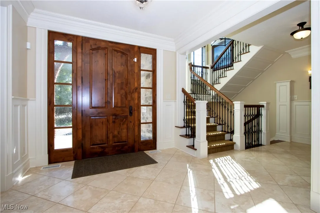 Foyer entrance featuring crown molding, a decorative wall, light tile patterned floors, a wainscoted wall, and stairs