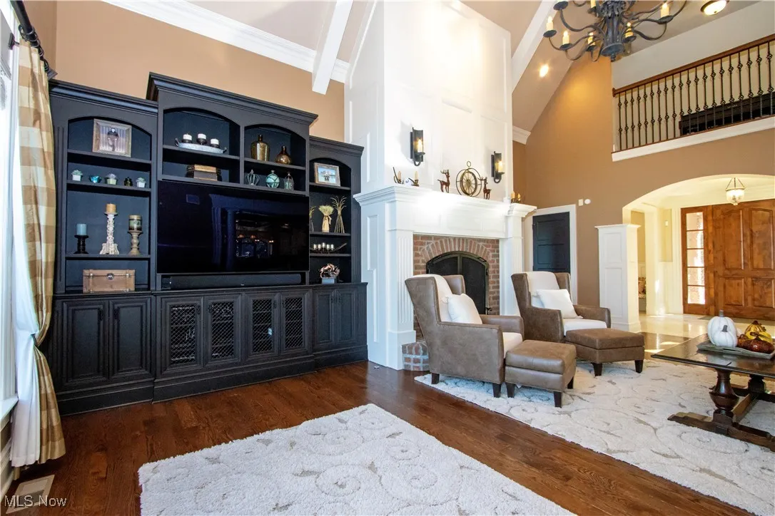 Living area with dark wood-style flooring, arched walkways, high vaulted ceiling, a brick fireplace, and a chandelier