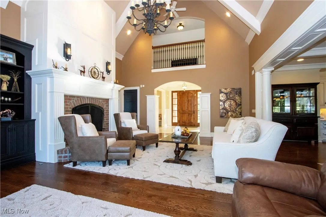 Living room with recessed lighting, dark wood-type flooring, ornamental molding, high vaulted ceiling, and a brick fireplace