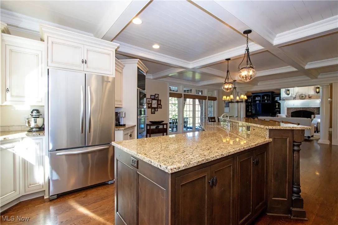Kitchen featuring dark brown cabinetry, appliances with stainless steel finishes, beamed ceiling, light stone counters, and a fireplace
