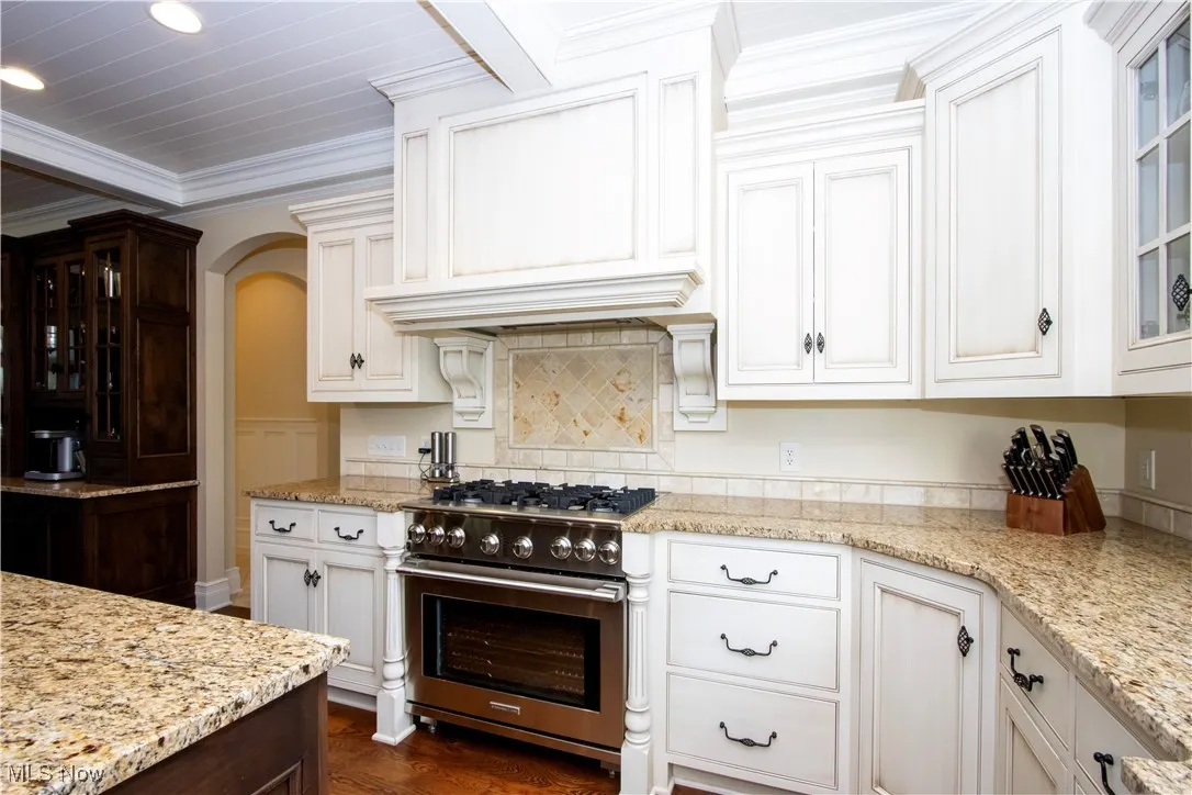 Kitchen with glass insert cabinets, gas stove, crown molding, light stone countertops, and white cabinetry