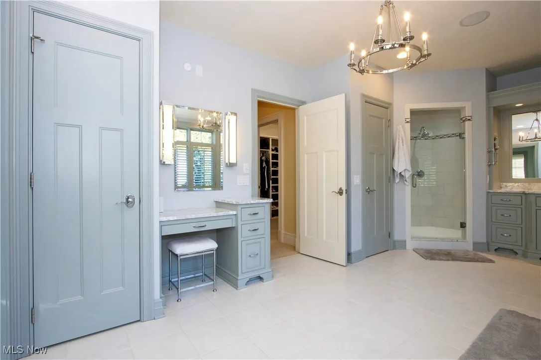 Full bathroom with a chandelier, vanity, a stall shower, light tile patterned flooring, and a spacious closet