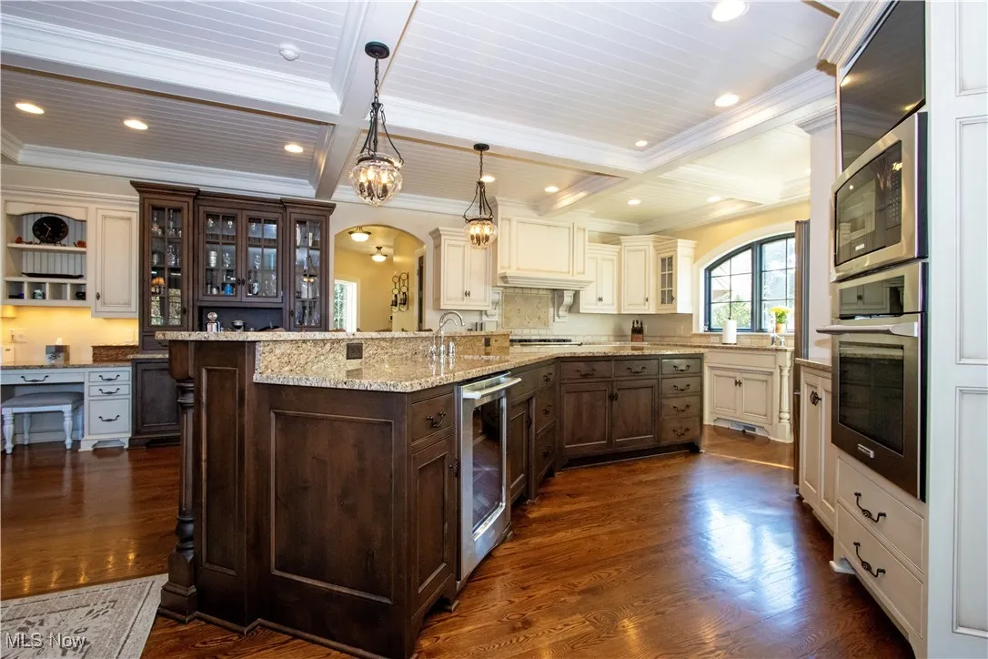 Kitchen featuring glass insert cabinets, arched walkways, dark brown cabinets, beamed ceiling, and coffered ceiling