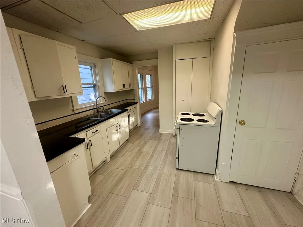 Kitchen featuring dark countertops, electric range, wood tiled floors, white cabinets, and a drop ceiling