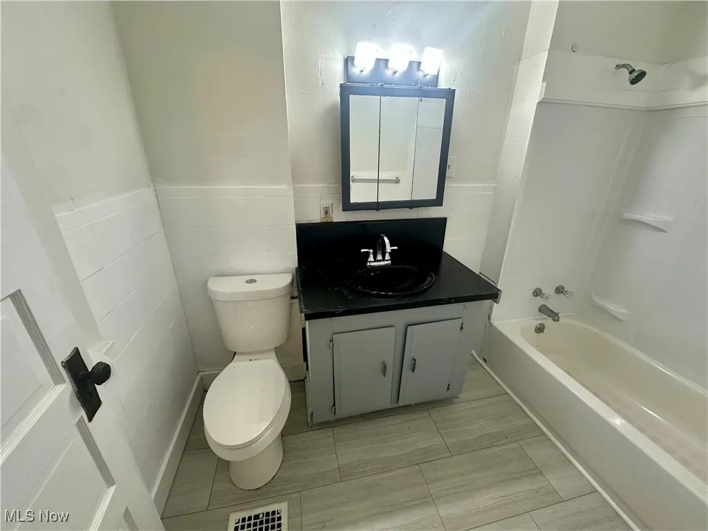 Bathroom featuring shower / bathtub combination, vanity, tile walls, and a wainscoted wall