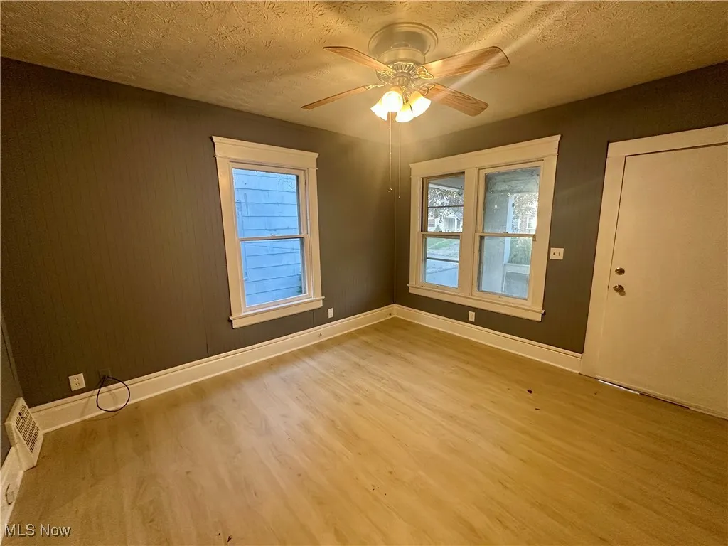 Empty room with a textured ceiling, light wood finished floors, a ceiling fan, and healthy amount of natural light