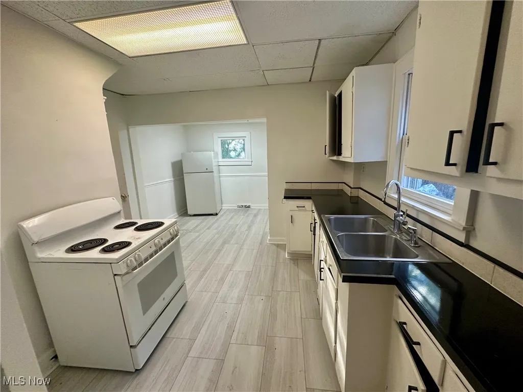 Kitchen with dark countertops, white appliances, white cabinetry, a drop ceiling, and wood tiled floors