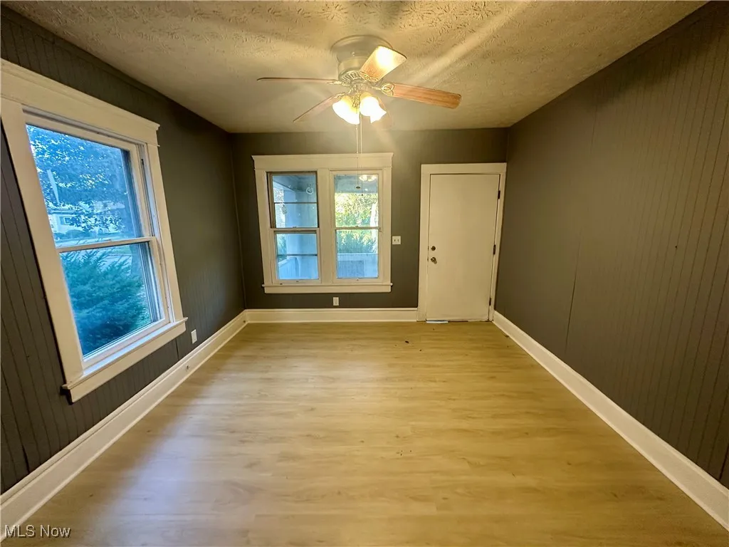 Spare room with a textured ceiling, light wood-style flooring, wooden walls, and a ceiling fan