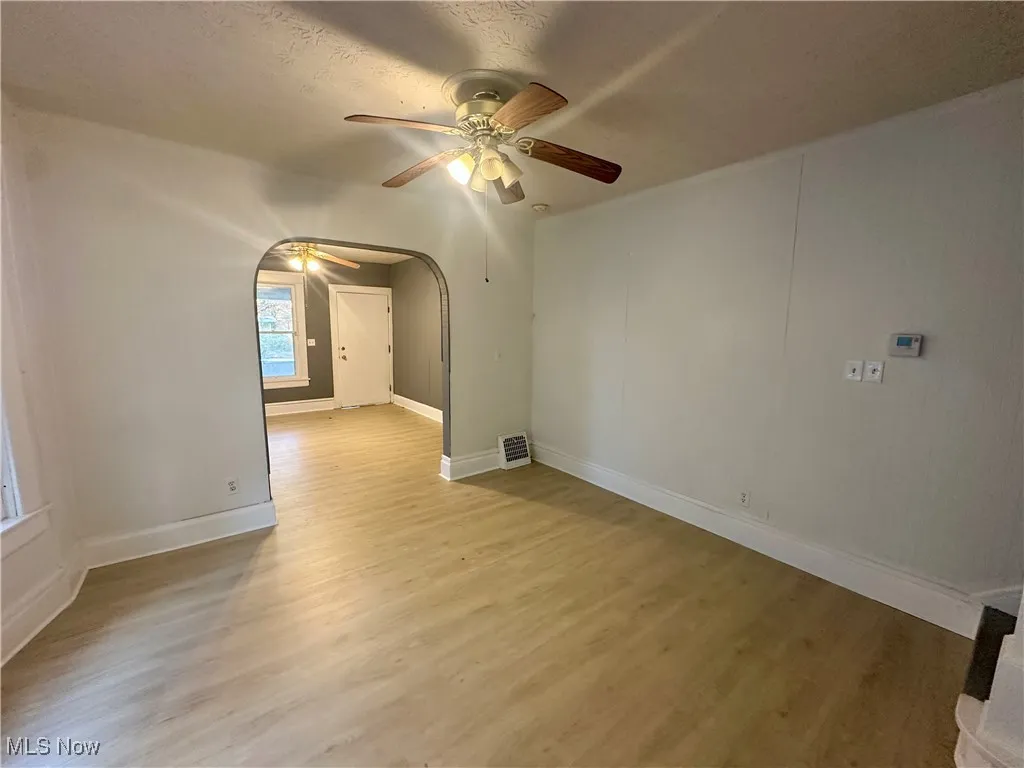 Spare room with arched walkways, light wood-type flooring, a ceiling fan, and a textured ceiling