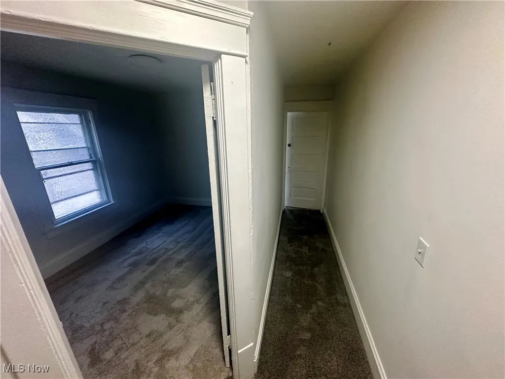 Corridor featuring dark colored carpet and baseboards