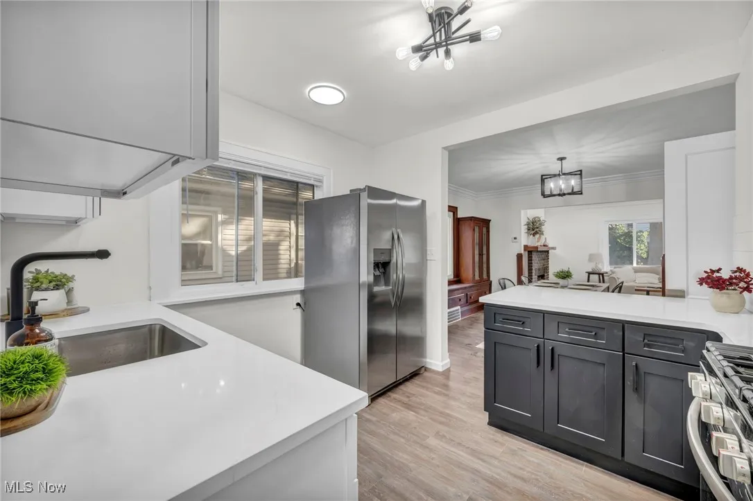 Kitchen featuring stainless steel appliances, a chandelier, light wood-style flooring, light stone counters, and a peninsula