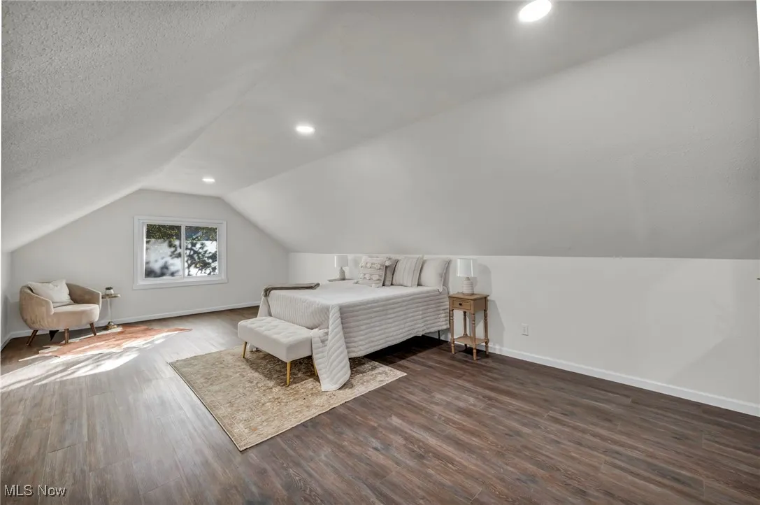Bedroom with dark wood-style flooring, lofted ceiling, and a textured ceiling