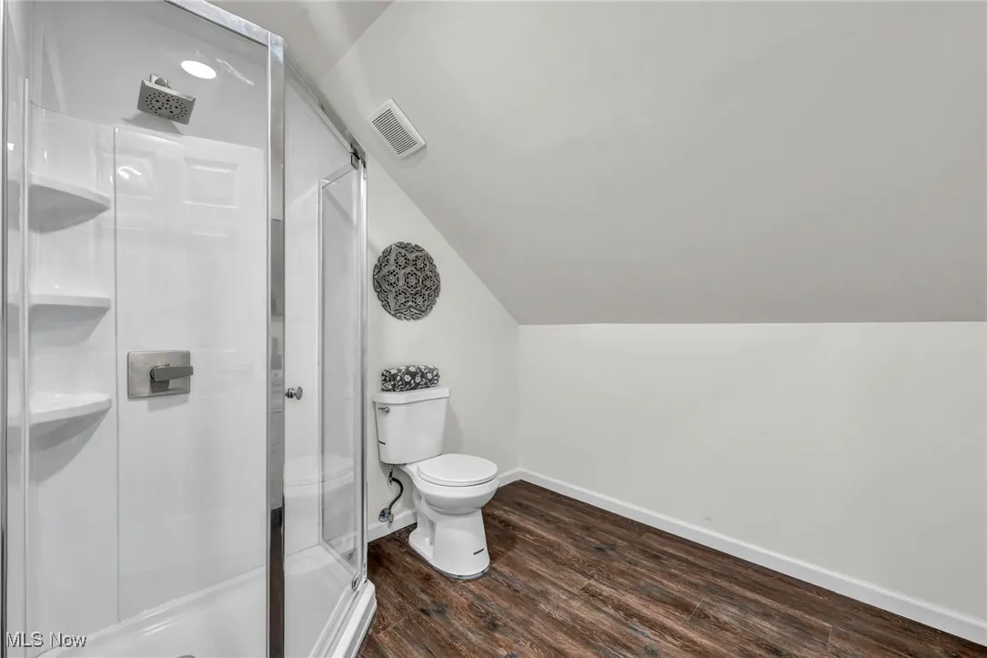 Full bath featuring dark wood-style flooring, vaulted ceiling, and a shower stall