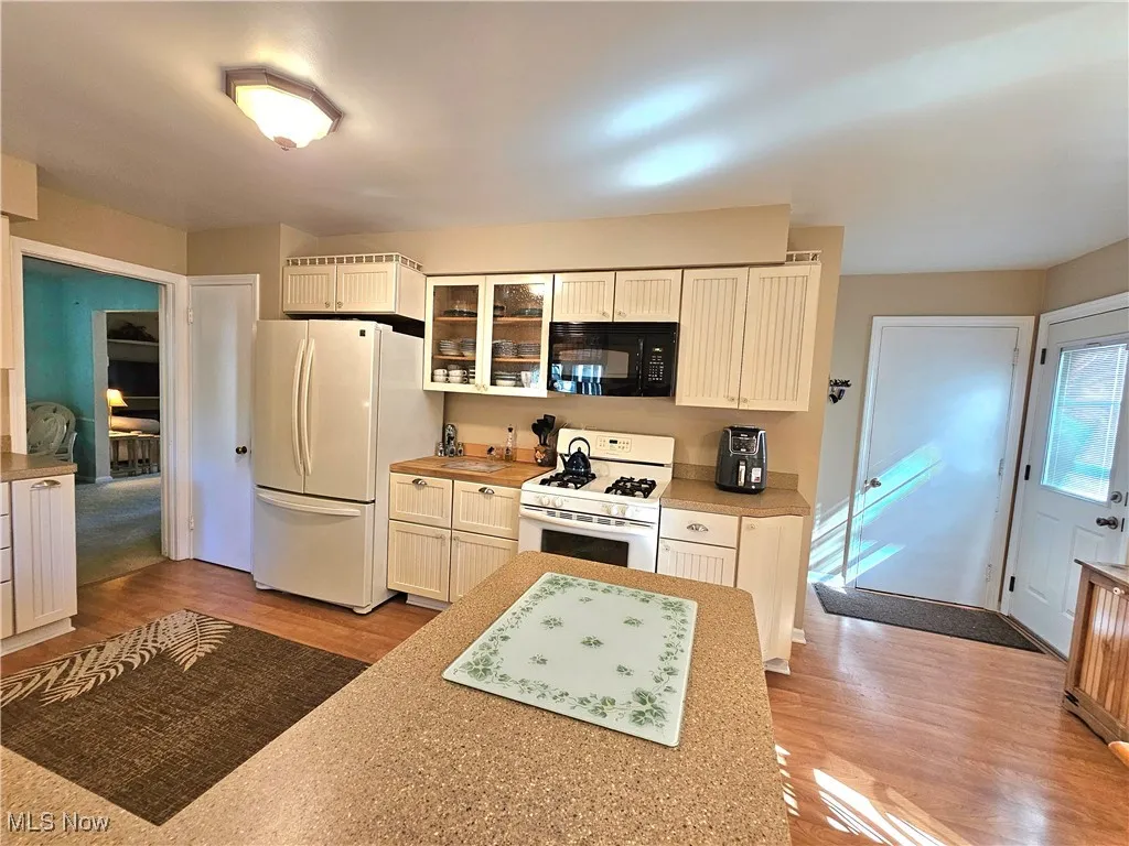 Kitchen with all appliances, light wood-style flooring, cream cabinets, glass insert cabinets, and light countertops