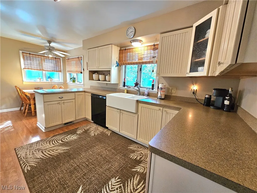 Eat in Kitchen featuring glass insert cabinets, wood finished floors, black dishwasher, a peninsula, and ceiling fan