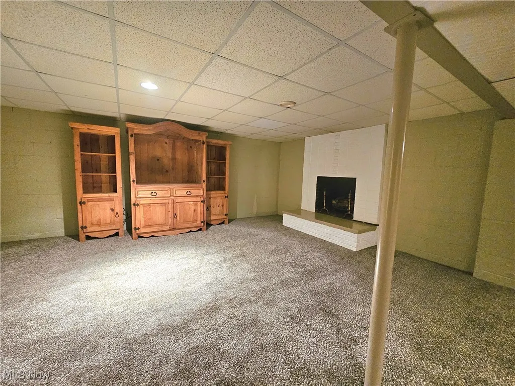 Unfurnished living room with carpet, a paneled ceiling, concrete block wall, a fireplace, and recessed lighting