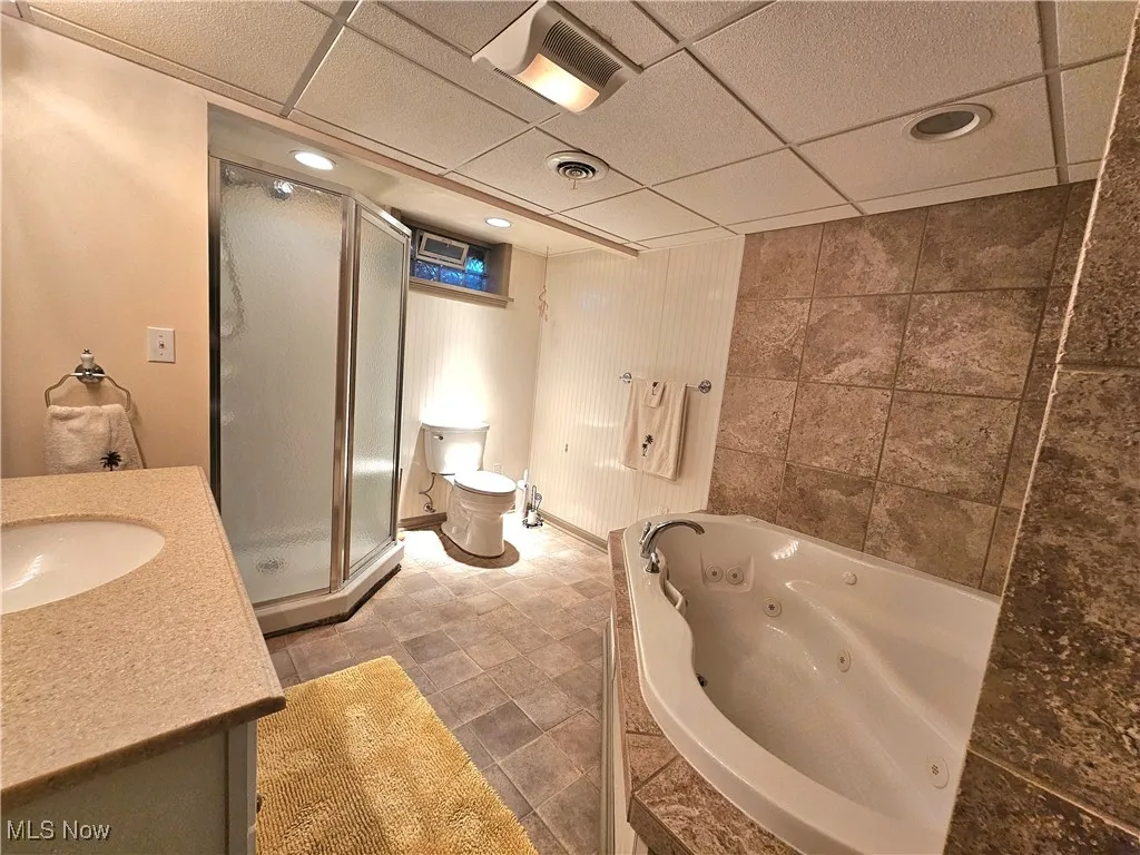 Full bath with a drop ceiling, vanity, a shower stall, a jetted tub, and tile walls
