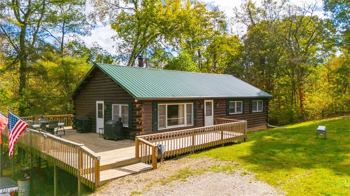 Rear view of house featuring log exterior, a deck, a metal roof, and a lawn
