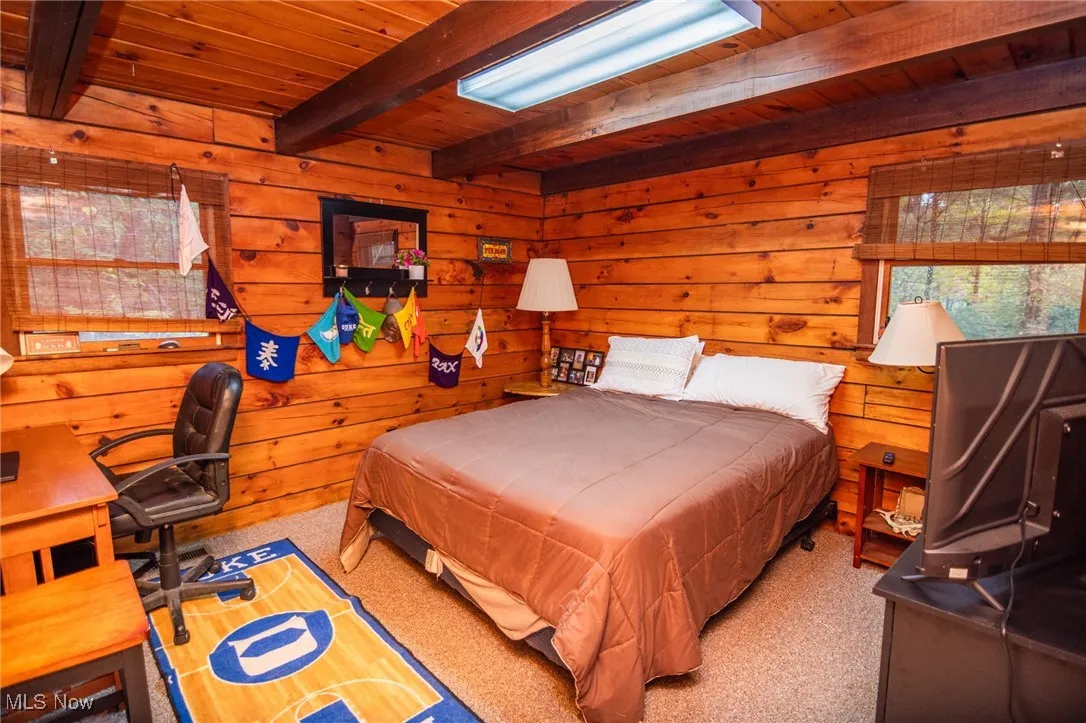 Carpeted bedroom with a wooden ceiling with exposed beams, an office area, and wooden walls