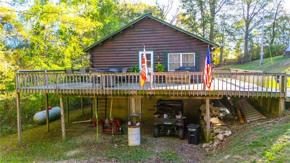 Rear view of house featuring a wooden deck, log siding, and view of wooded area