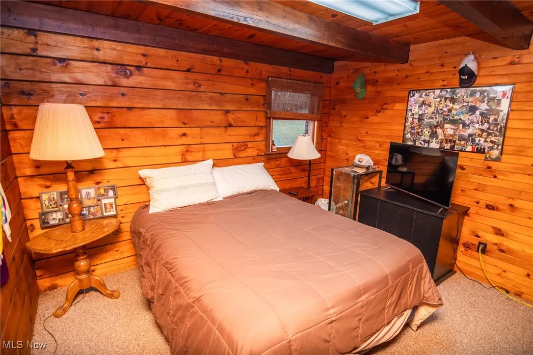 Bedroom with carpet, a wooden ceiling with exposed beams, and wooden walls