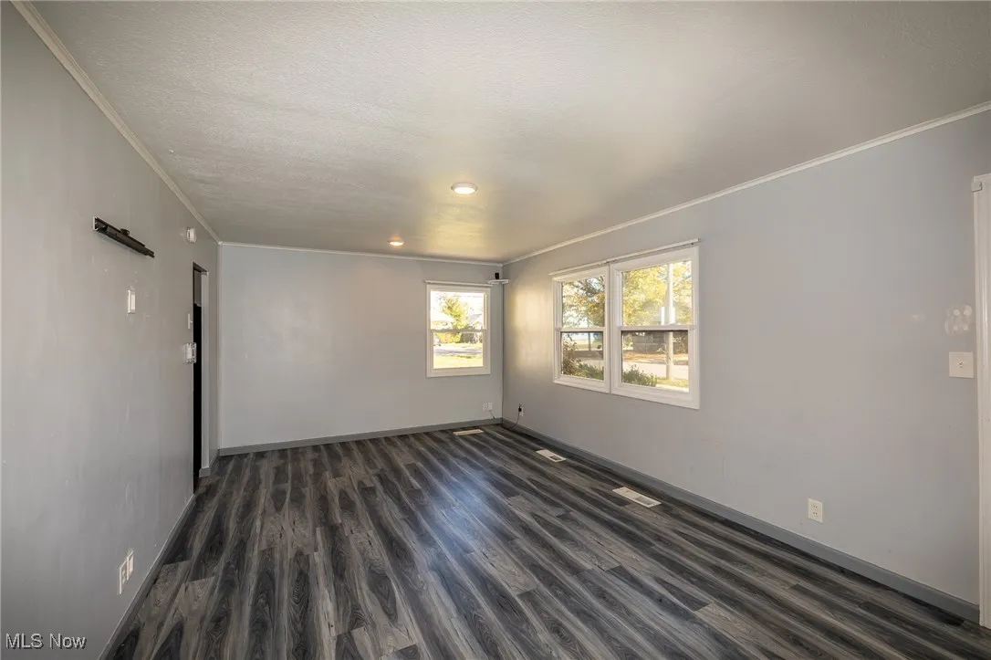 Unfurnished room featuring crown molding, dark wood-style flooring, and a textured ceiling