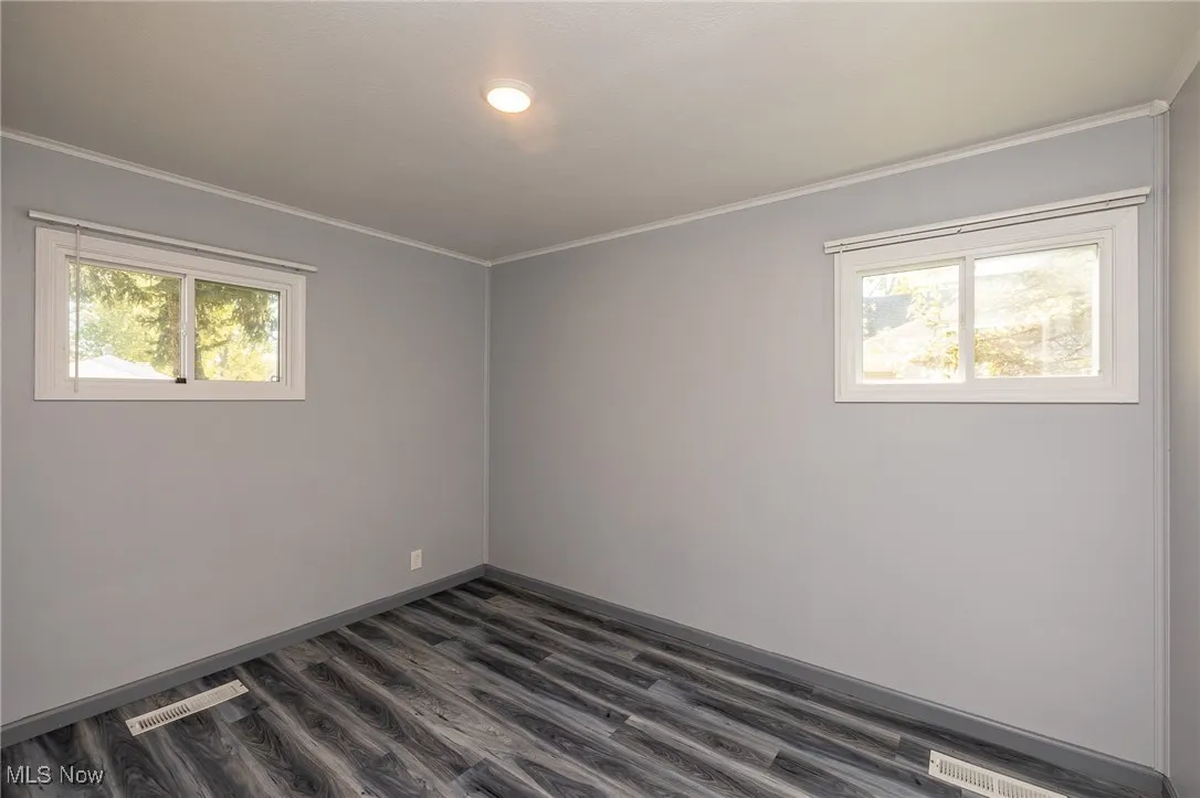 Unfurnished room with healthy amount of natural light, dark wood-type flooring, and ornamental molding