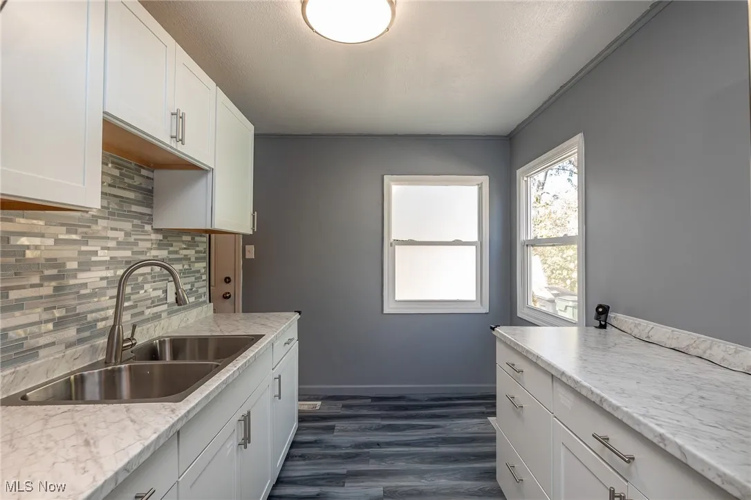 Kitchen with decorative backsplash, white cabinetry, and dark wood-style flooring