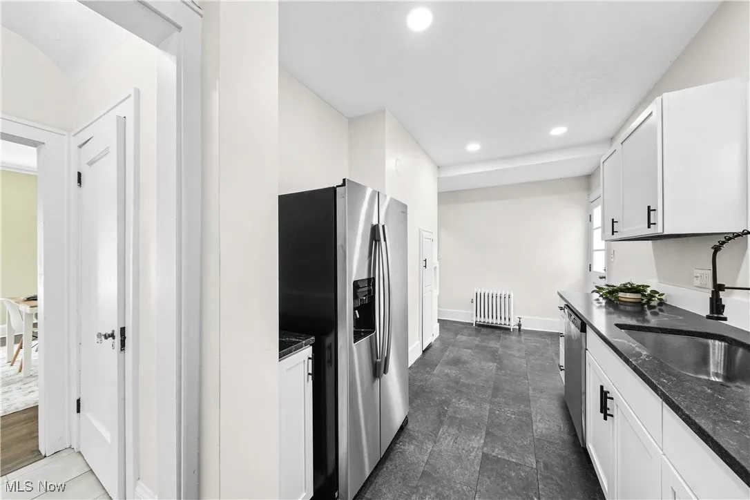 Kitchen with appliances with stainless steel finishes, white cabinets, recessed lighting, dark stone counters, and radiator