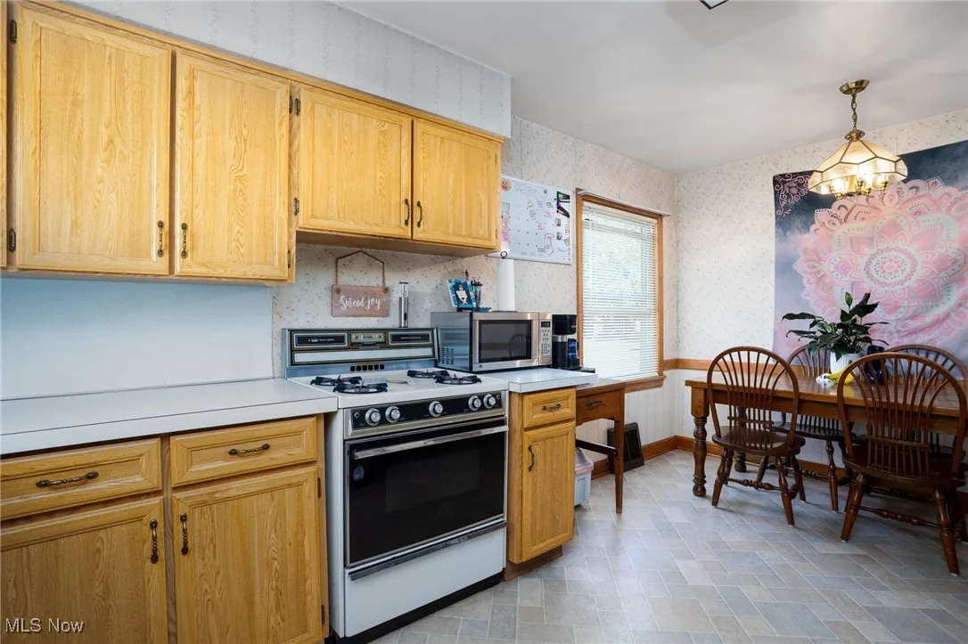 Kitchen with light countertops, wallpapered walls, white range with gas cooktop, stainless steel microwave, and light brown cabinets