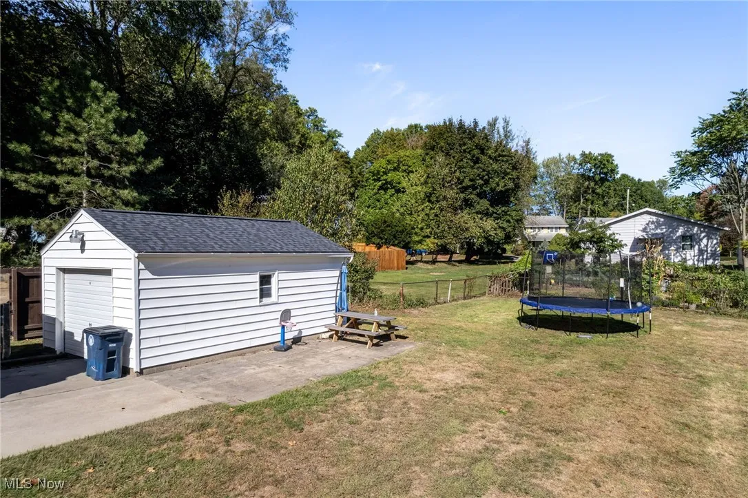 View of yard featuring a trampoline, a detached garage, an outbuilding, and a patio area