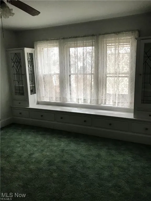 Spare room featuring plenty of natural light, dark colored carpet, and ceiling fan