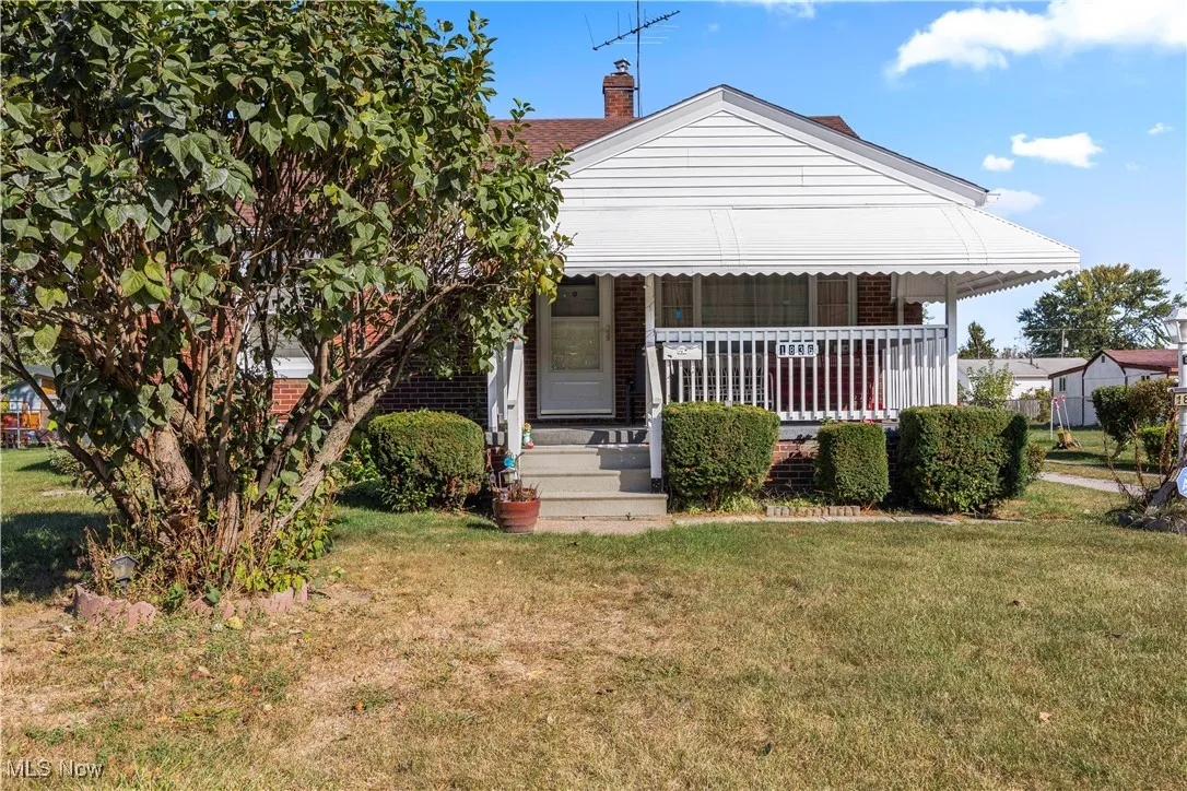 Bungalow-style home with a porch, a front yard, a chimney, and brick siding