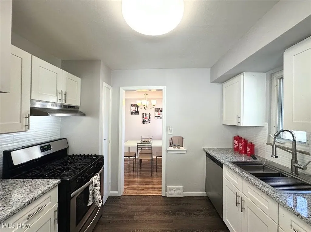 Kitchen featuring decorative backsplash, appliances with stainless steel finishes, dark wood finished floors, and white cabinetry
