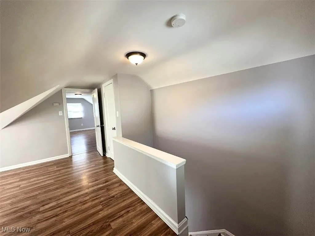 Corridor with an upstairs landing, dark wood-style flooring, and vaulted ceiling