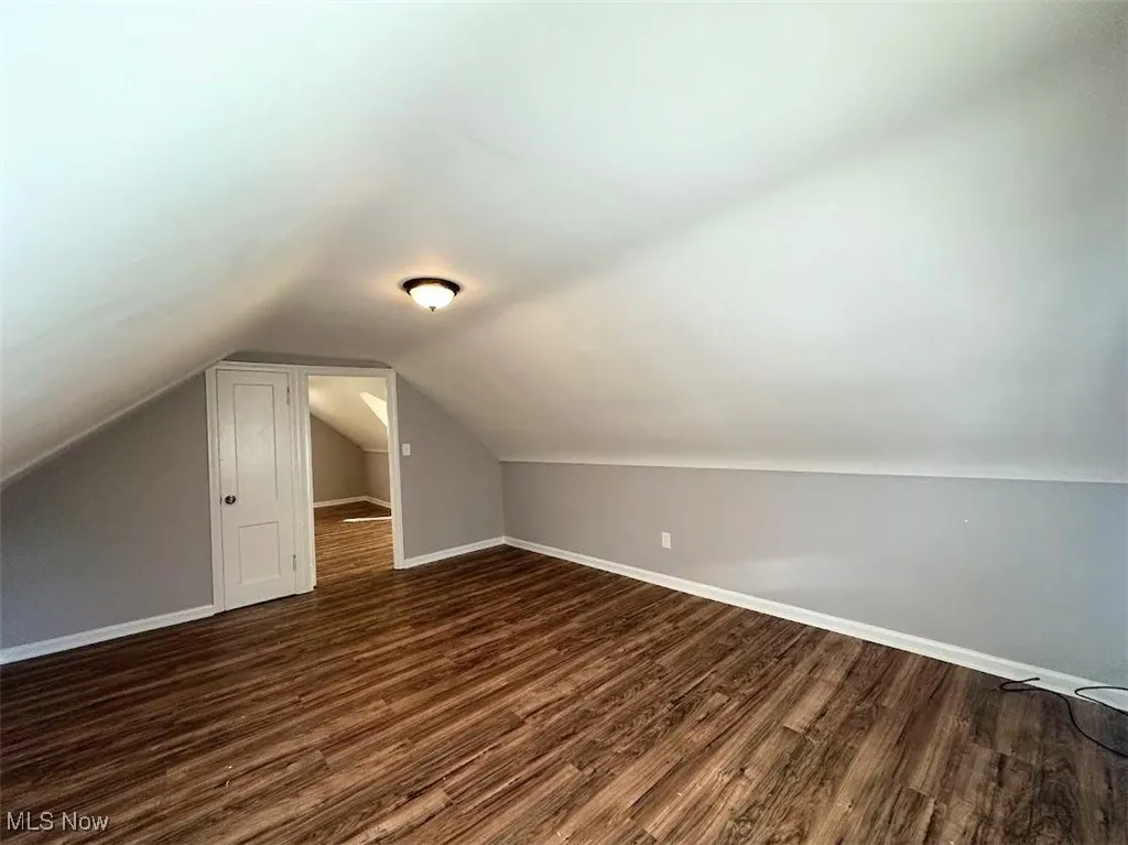 Additional living space featuring vaulted ceiling and dark wood-type flooring