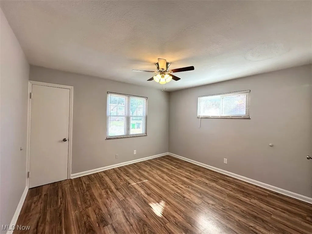 Unfurnished room with dark wood-type flooring, healthy amount of natural light, a textured ceiling, and a ceiling fan