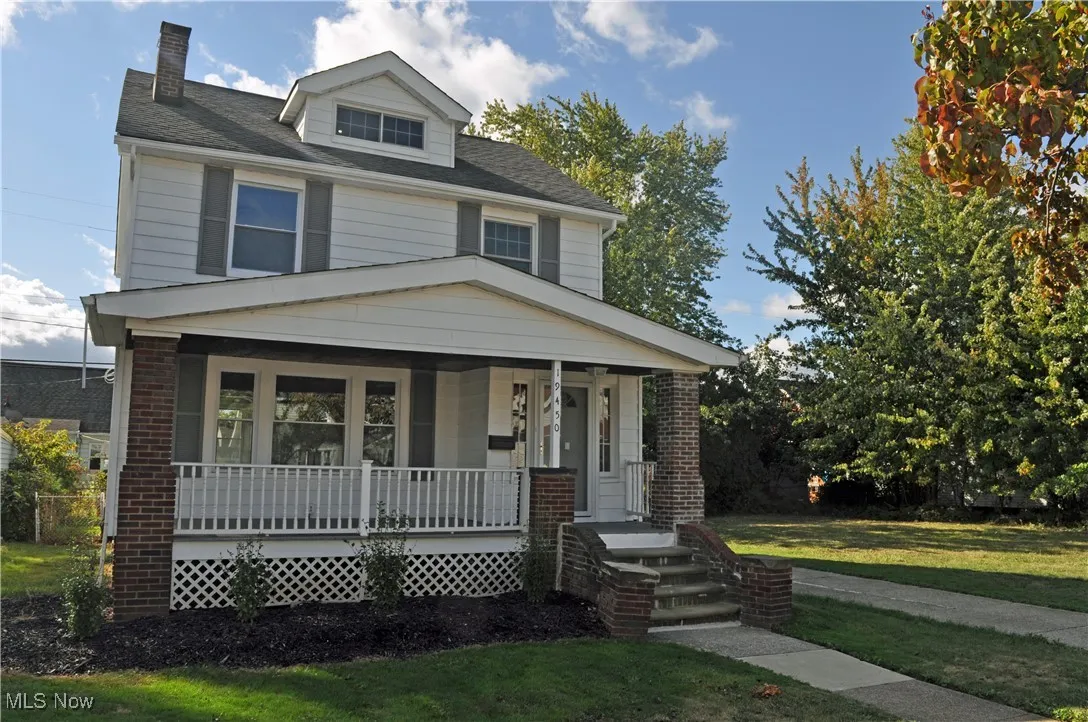 Traditional style home with covered porch, a chimney, a front yard, and roof with shingles