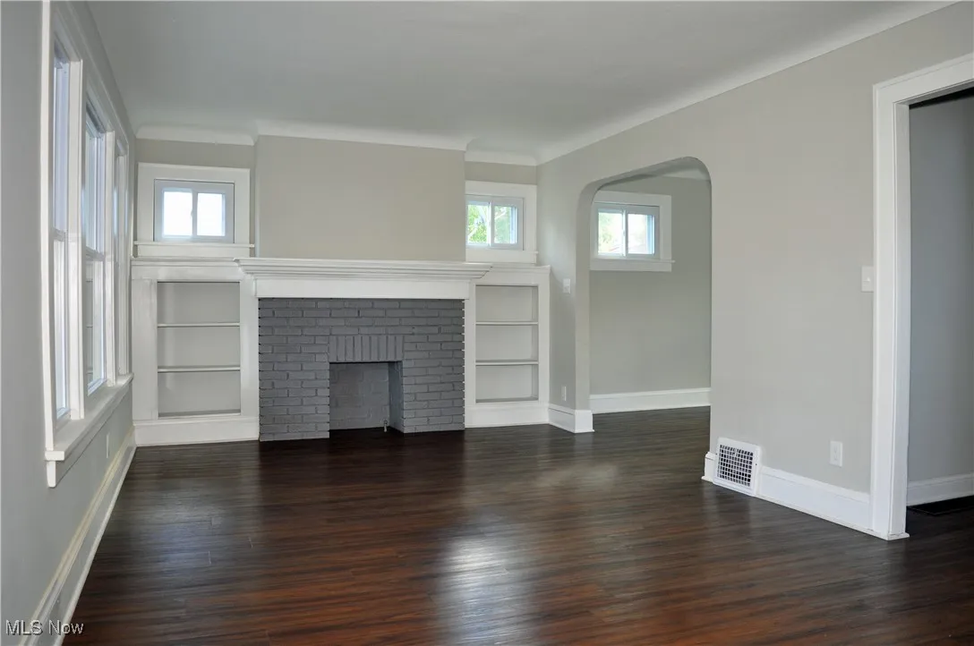 Unfurnished living room featuring arched walkways, dark wood-style floors, healthy amount of natural light, and a fireplace