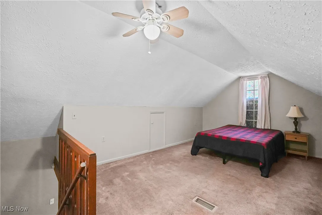 Bedroom with a textured ceiling, carpet, a ceiling fan, and lofted ceiling